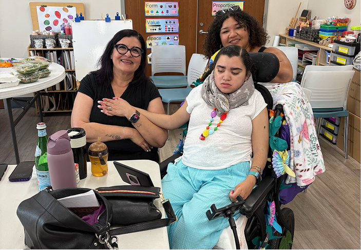 Two caregivers assist a child with Rett syndrome in a classroom