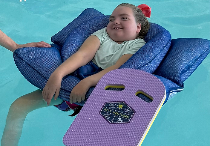 Child living with Rett syndrome floats in a pool during a community event