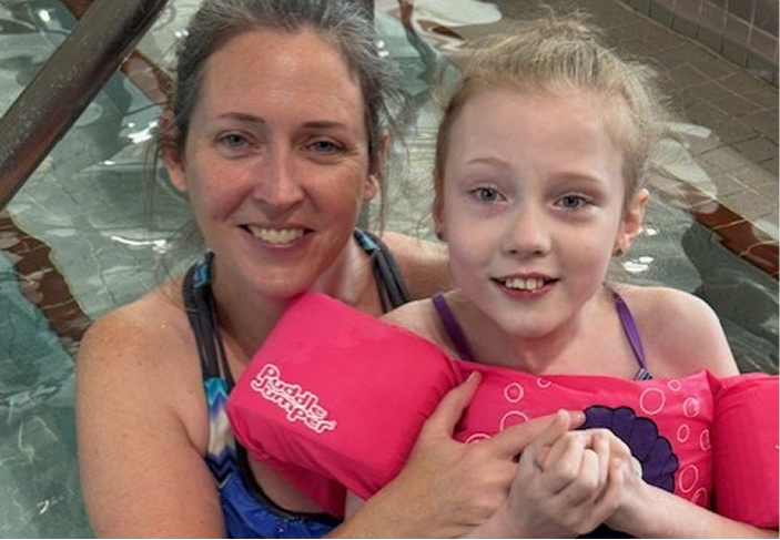 Caregiver holds a child with Rett syndrome during a community pool event