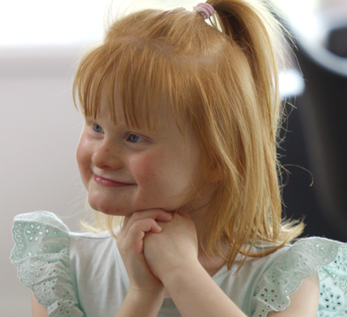 Minna smiling with her hands underneath her chin, looking away from camera